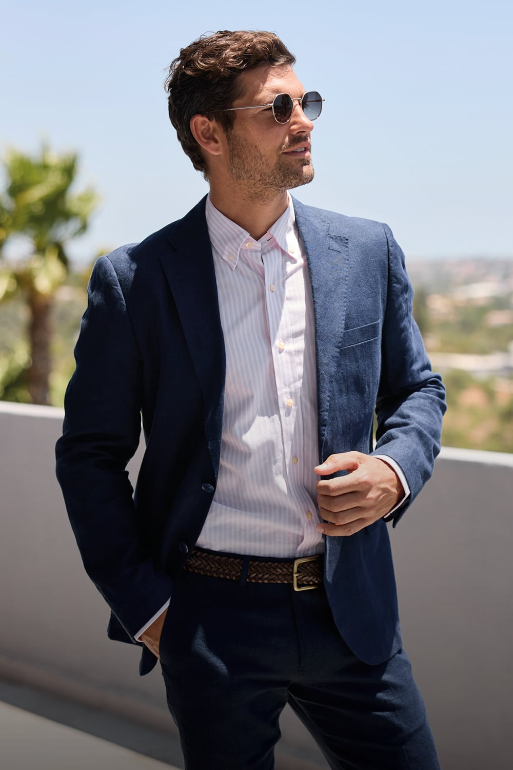 Man wearing a navy blazer over a white shirt with sunglasses, standing outdoors.