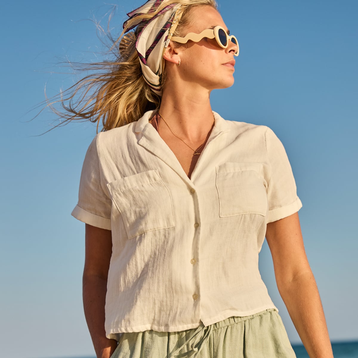 Woman wearing a beige shirt and sunglasses with a blue sky background