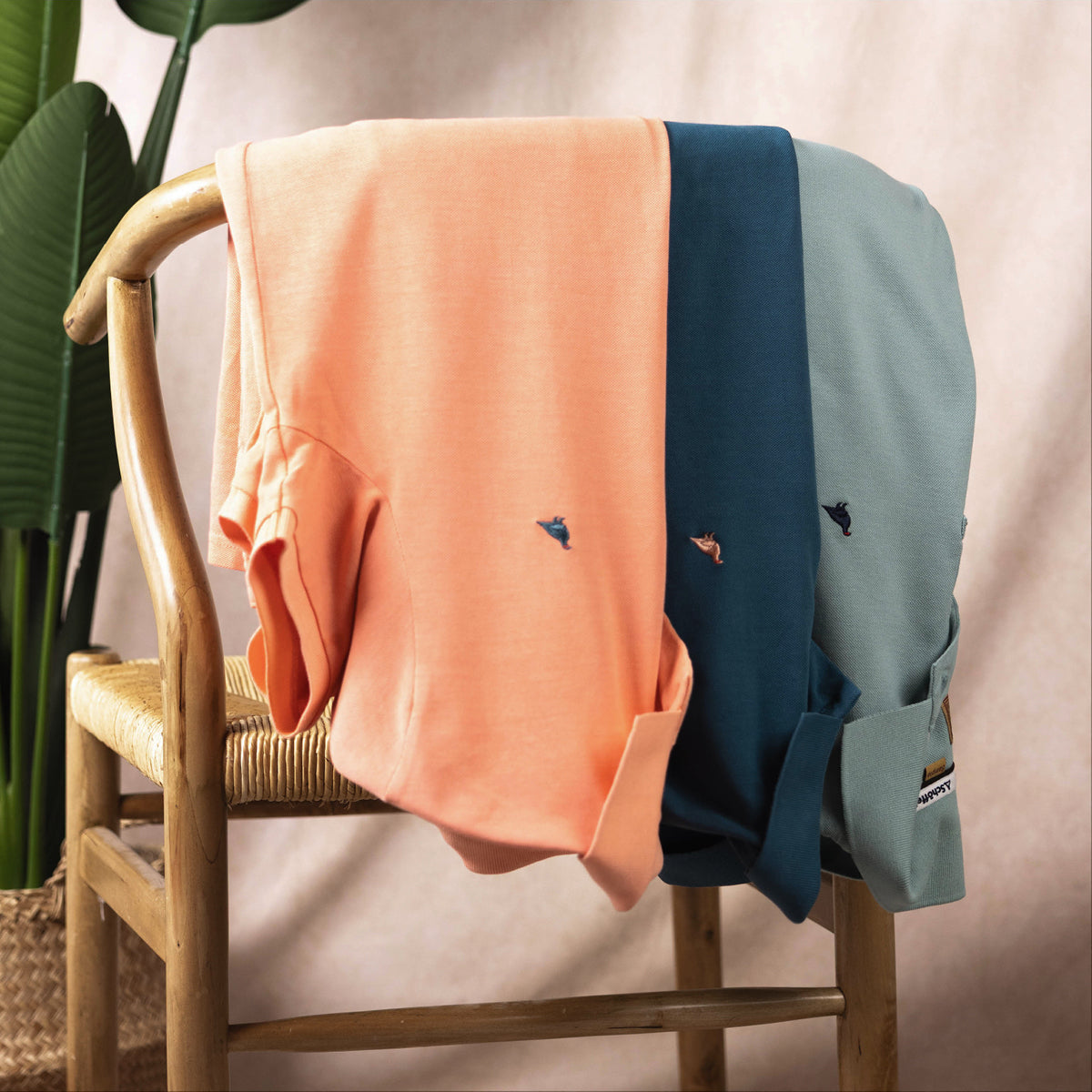 Two polos, one peach and one blue, draped over a chair with a plant in the background.