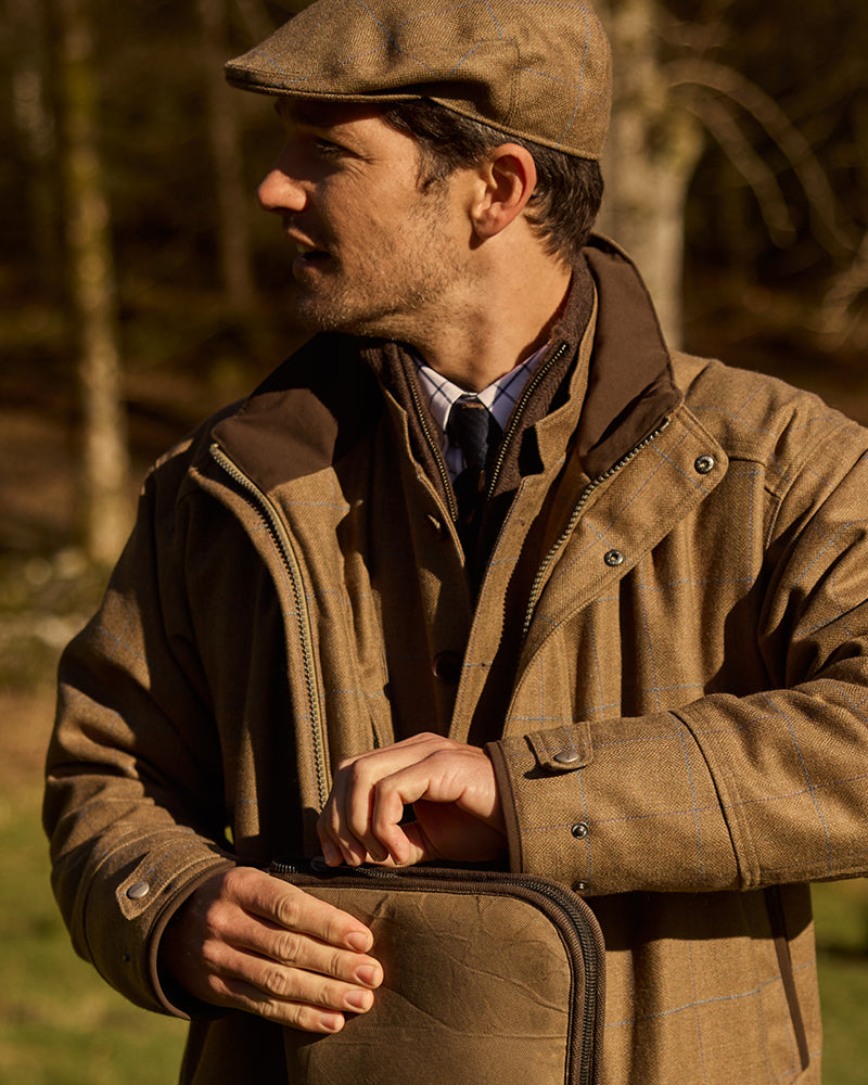 Man wearing a brown jacket and flat cap outdoors with a blurred natural background