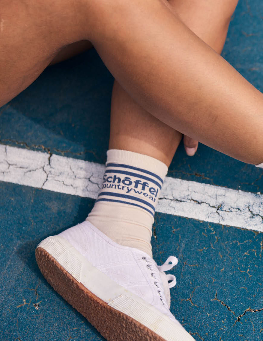 Person wearing white sneakers with brown soles on a blue surface