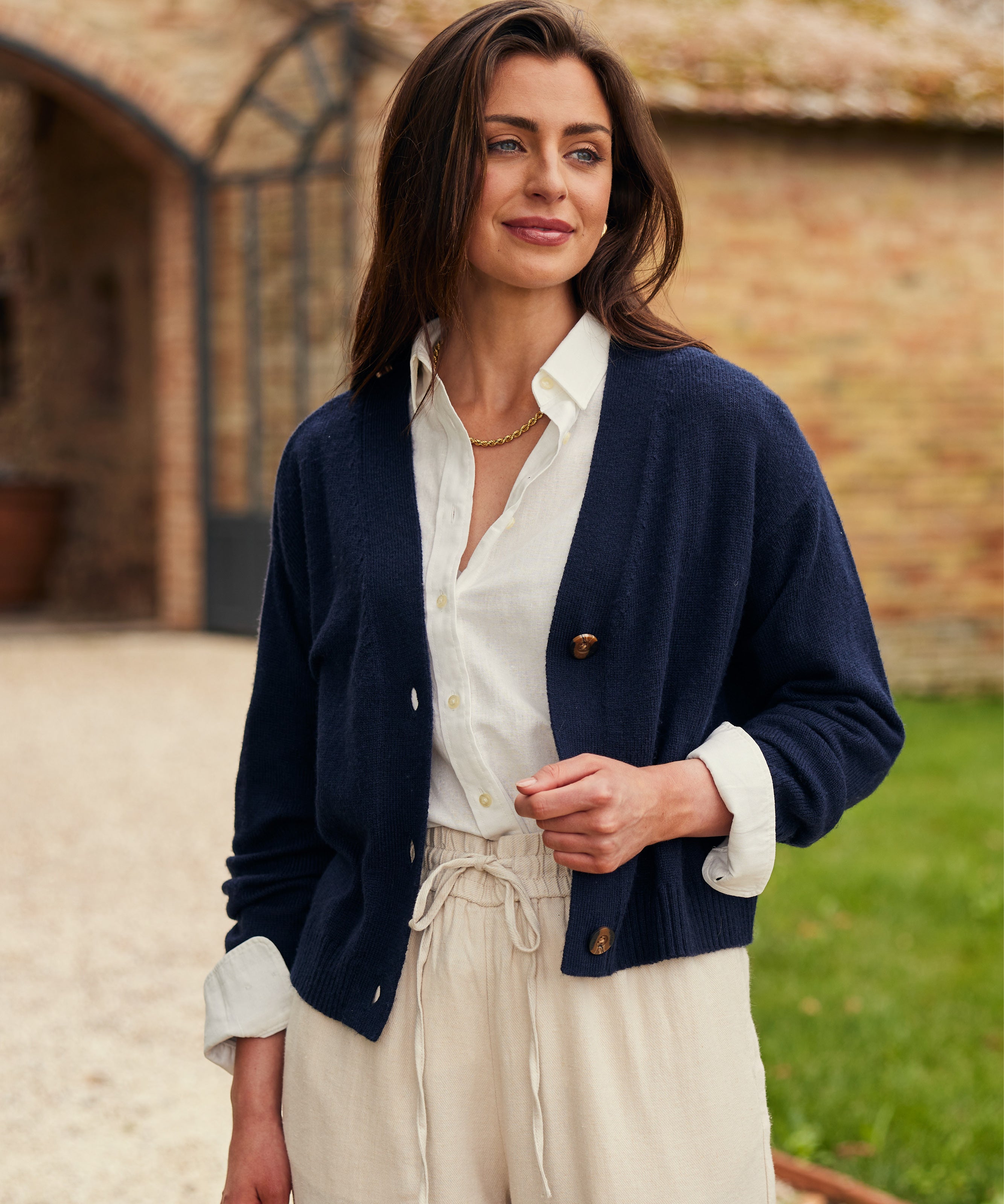 Woman wearing a dark blue cardigan and white shirt, with a gold necklace.