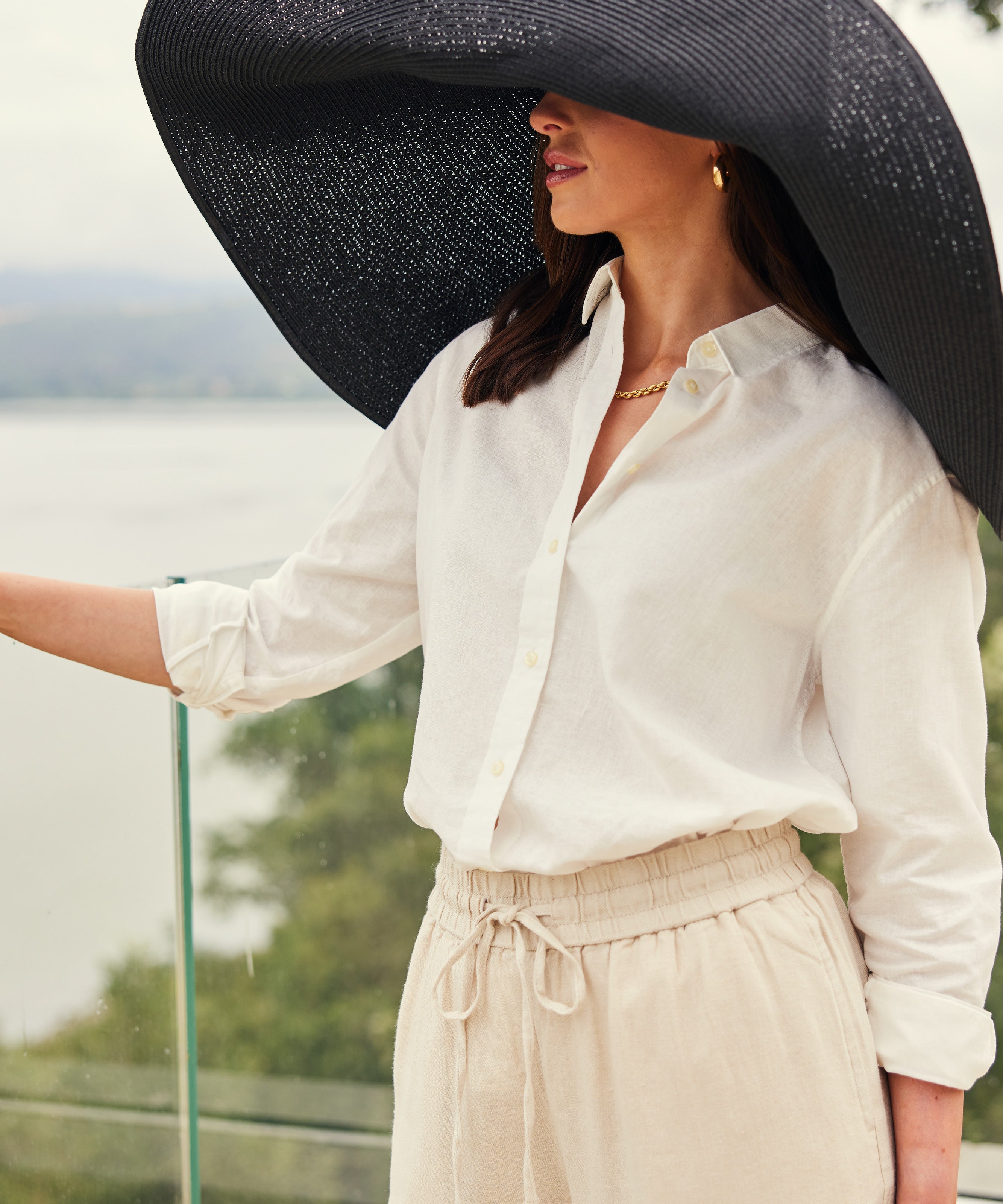 Woman in a large sun hat and white shirt, looking out over water.