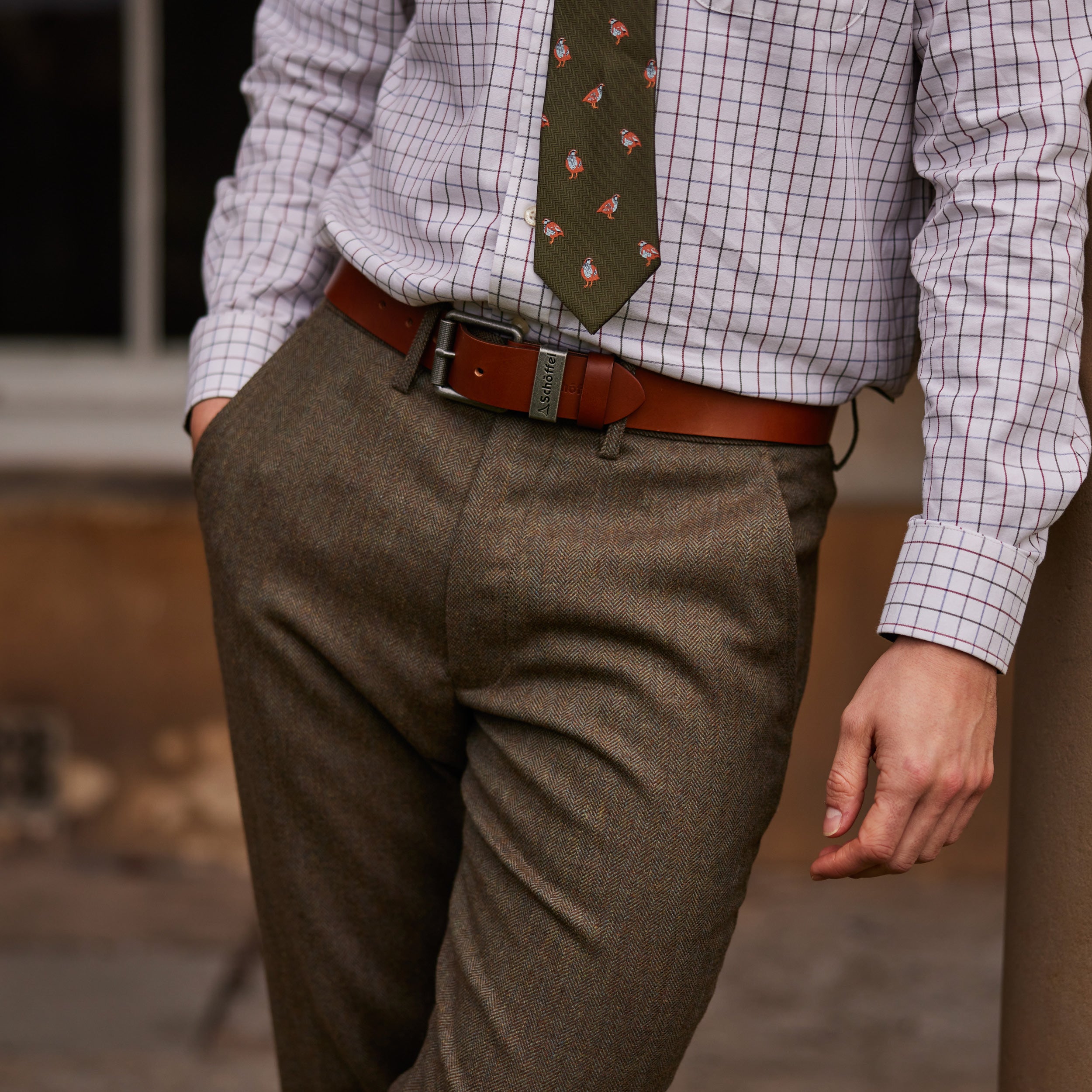 Tweed trousers with a tan leather belt, paired with a checked shirt and green patterned tie.