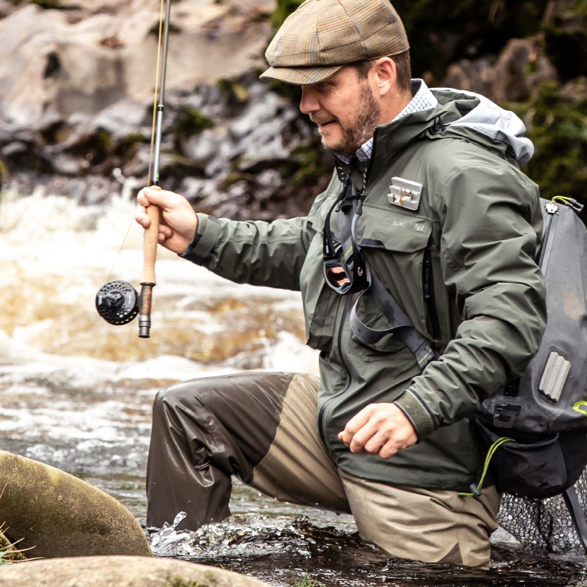 A man in a river holding a fishing rod and wearing fly fishing clothing.