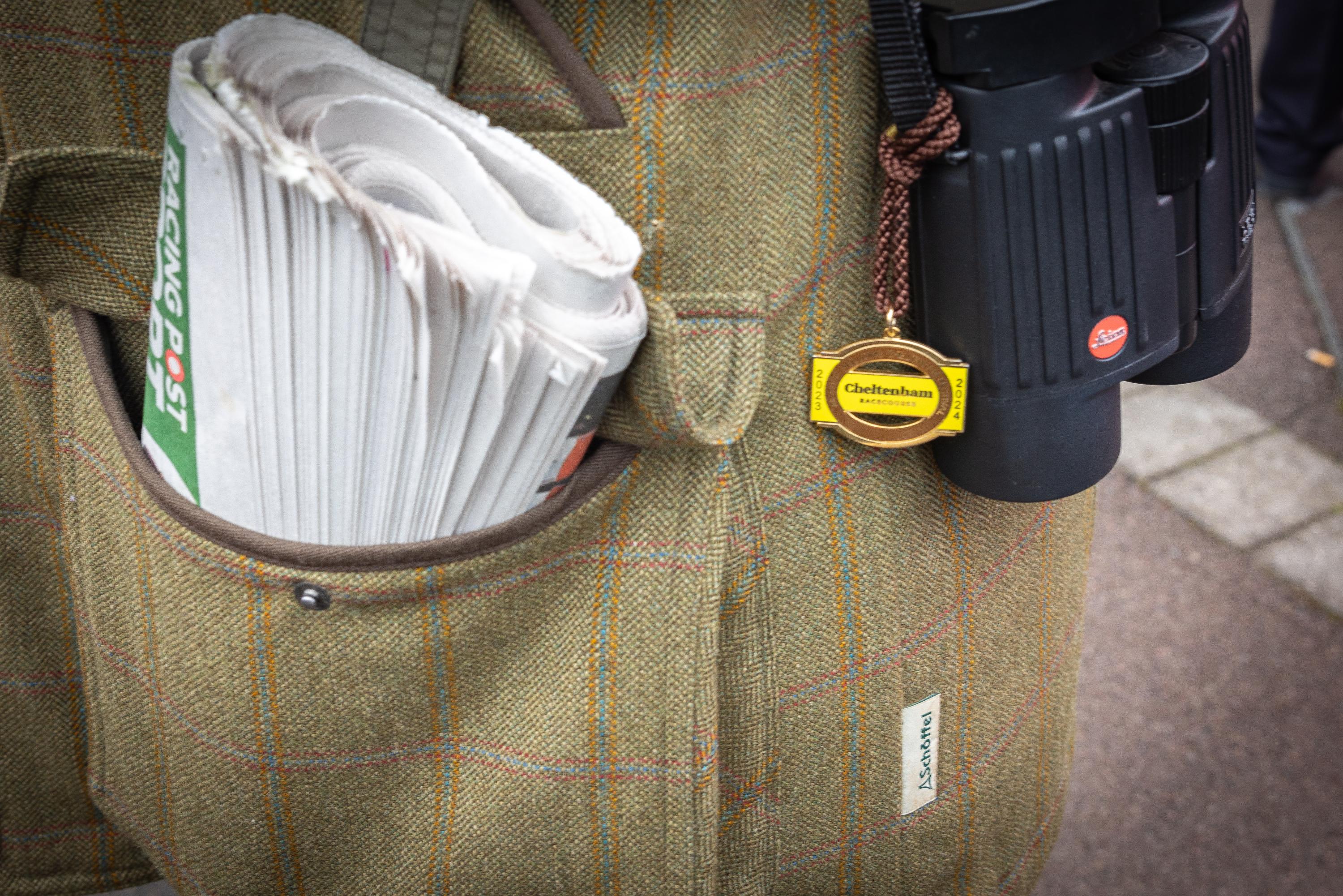 A close up image of a tweed Schöffel coat with a racing newspaper in the pocket and binoculars.