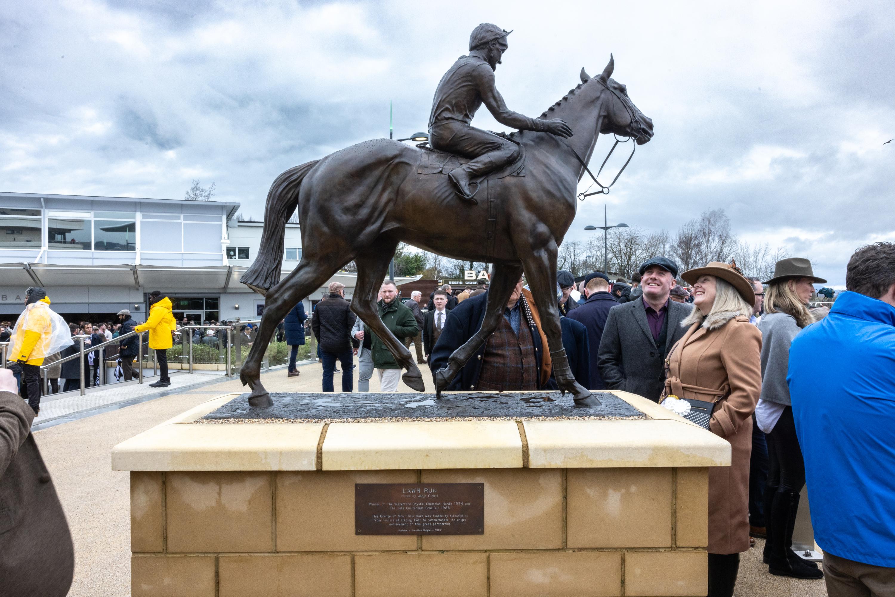 An image of a bronze racehorse and jockey statue with people looking on.