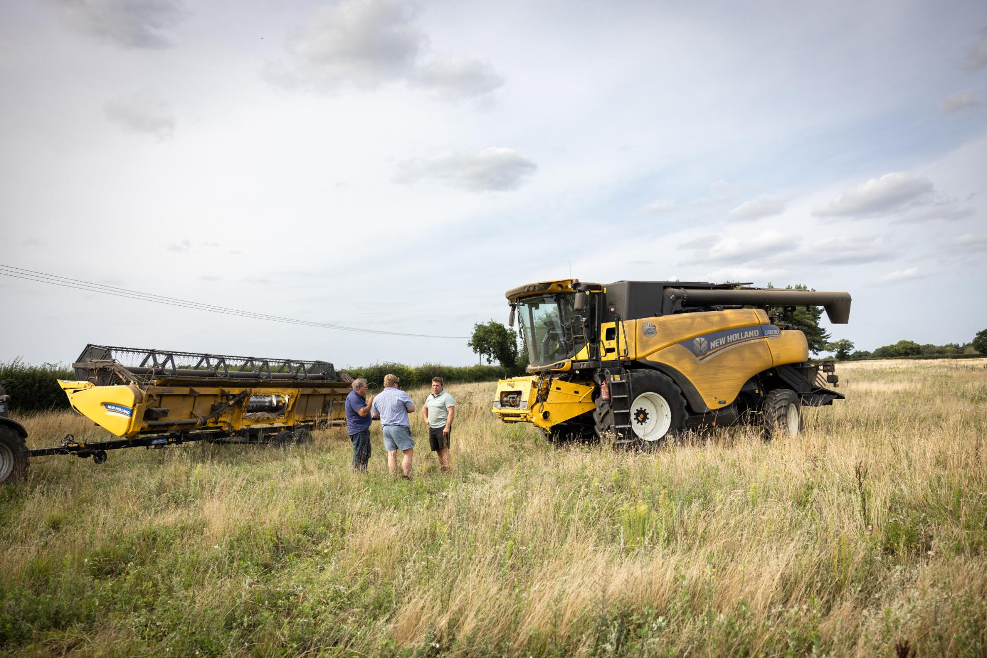 Harvester in a field with people observing, under a cloudy sky.