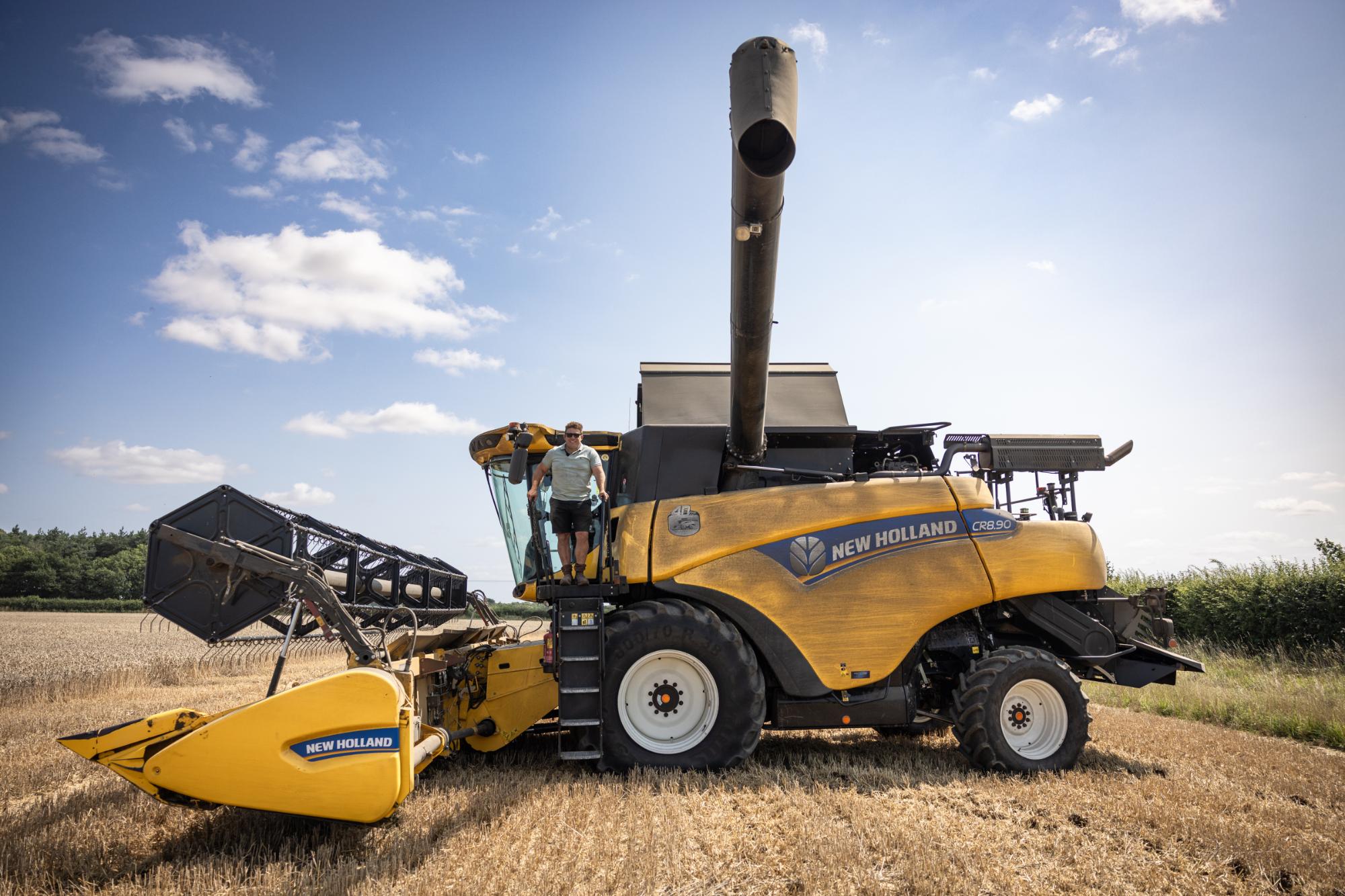 Yellow New Holland combine harvester in a field with a clear sky.