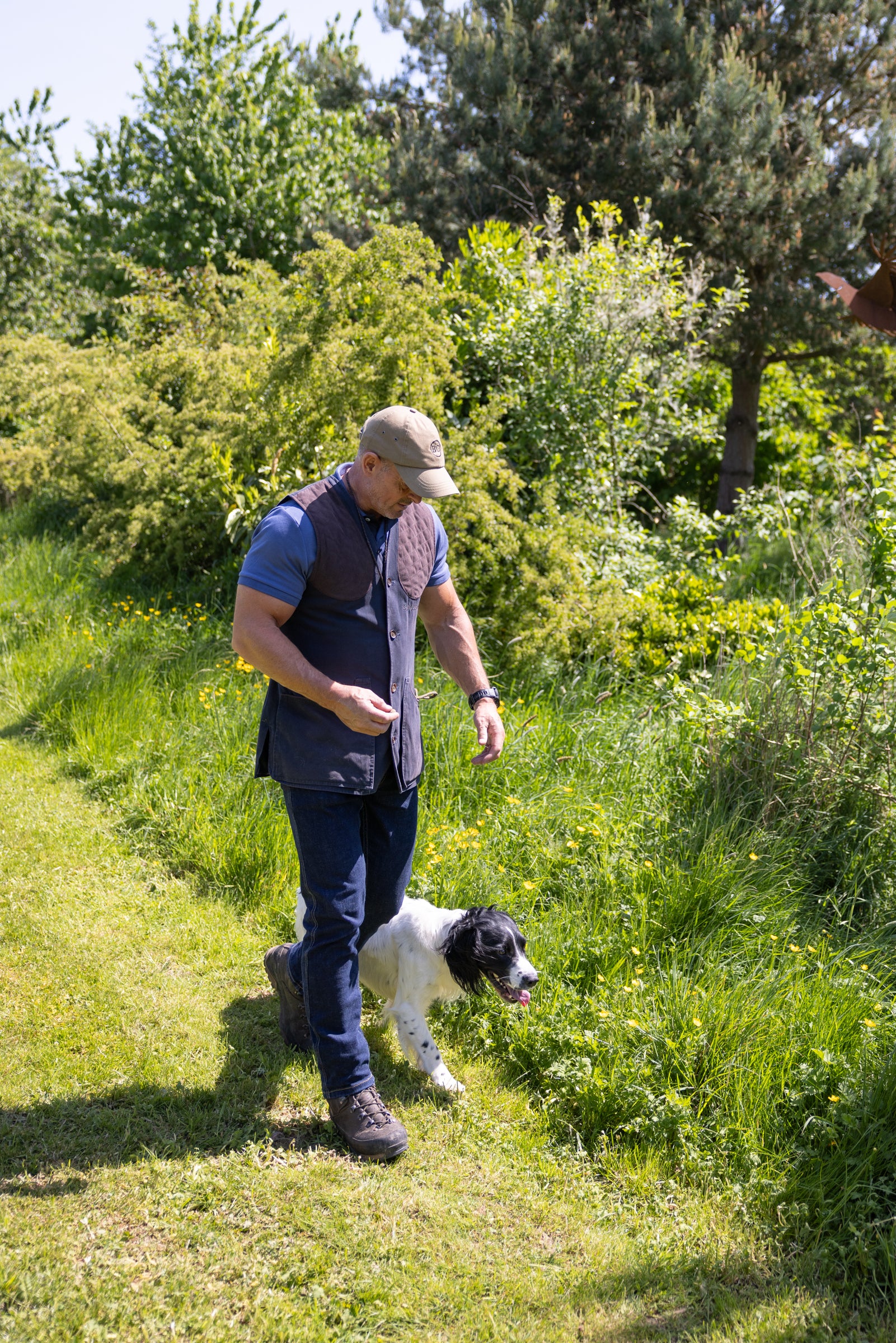 Man walking a dog on a grassy path with trees in the background