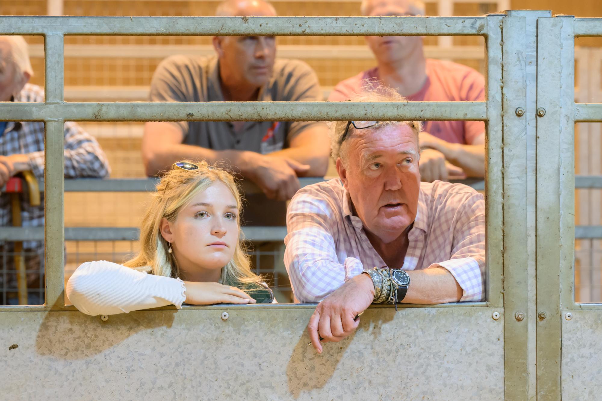 People looking through a metal fence at an event, with a focus on a woman and a man.
