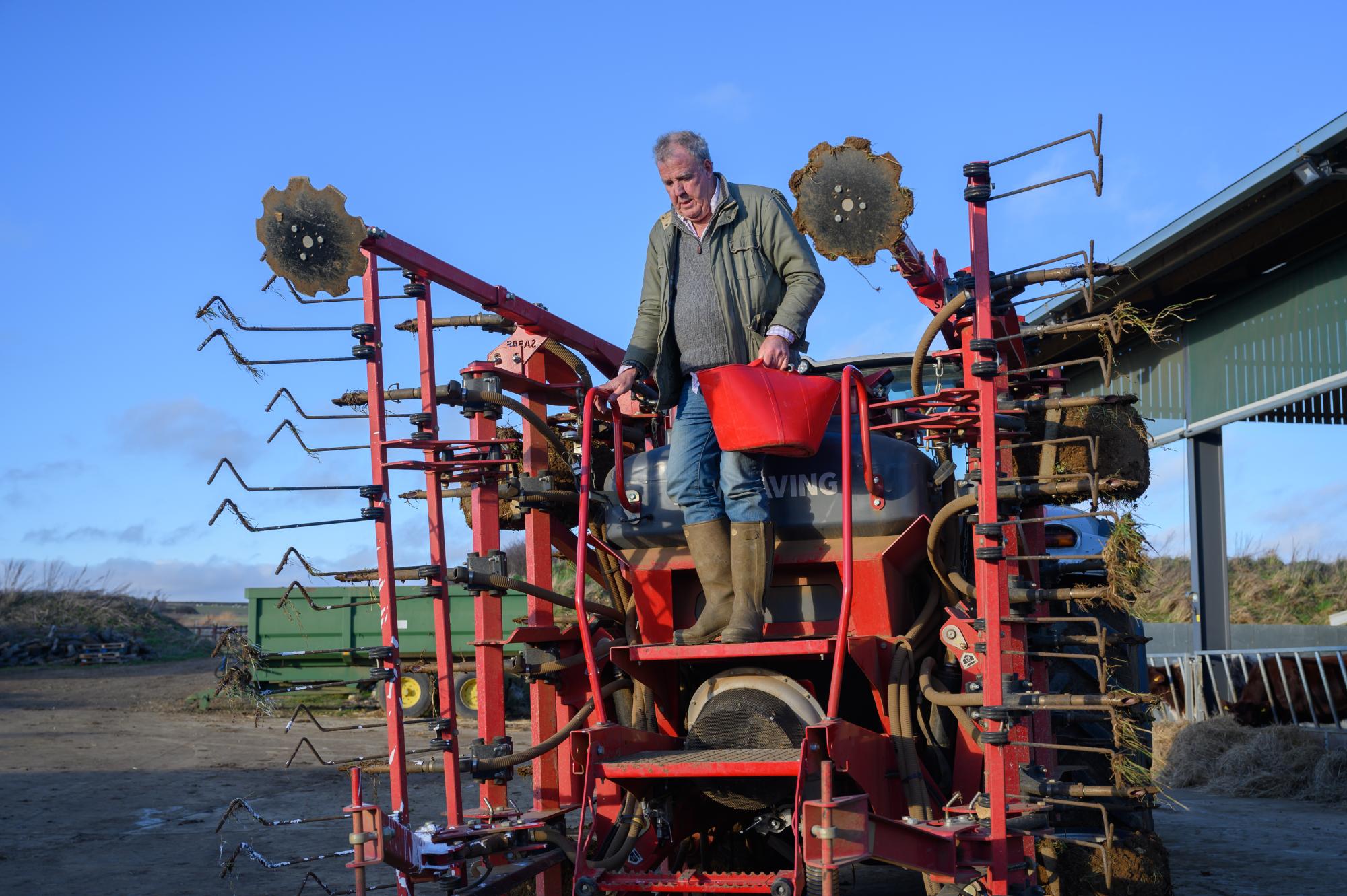 Man operating a large agricultural machine on a farm with a clear blue sky.