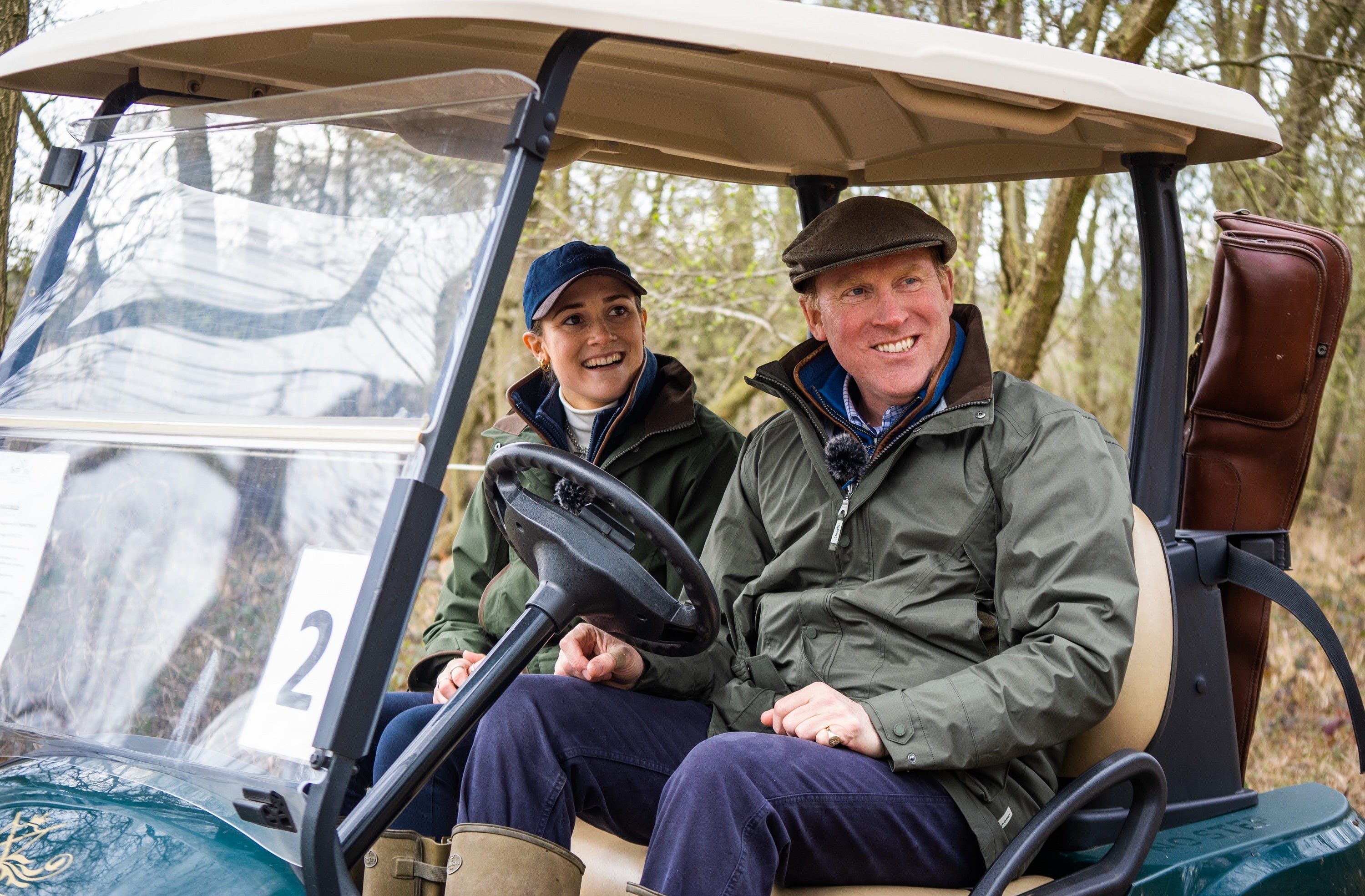 Two people sitting in a golf cart on a trail with trees in the background