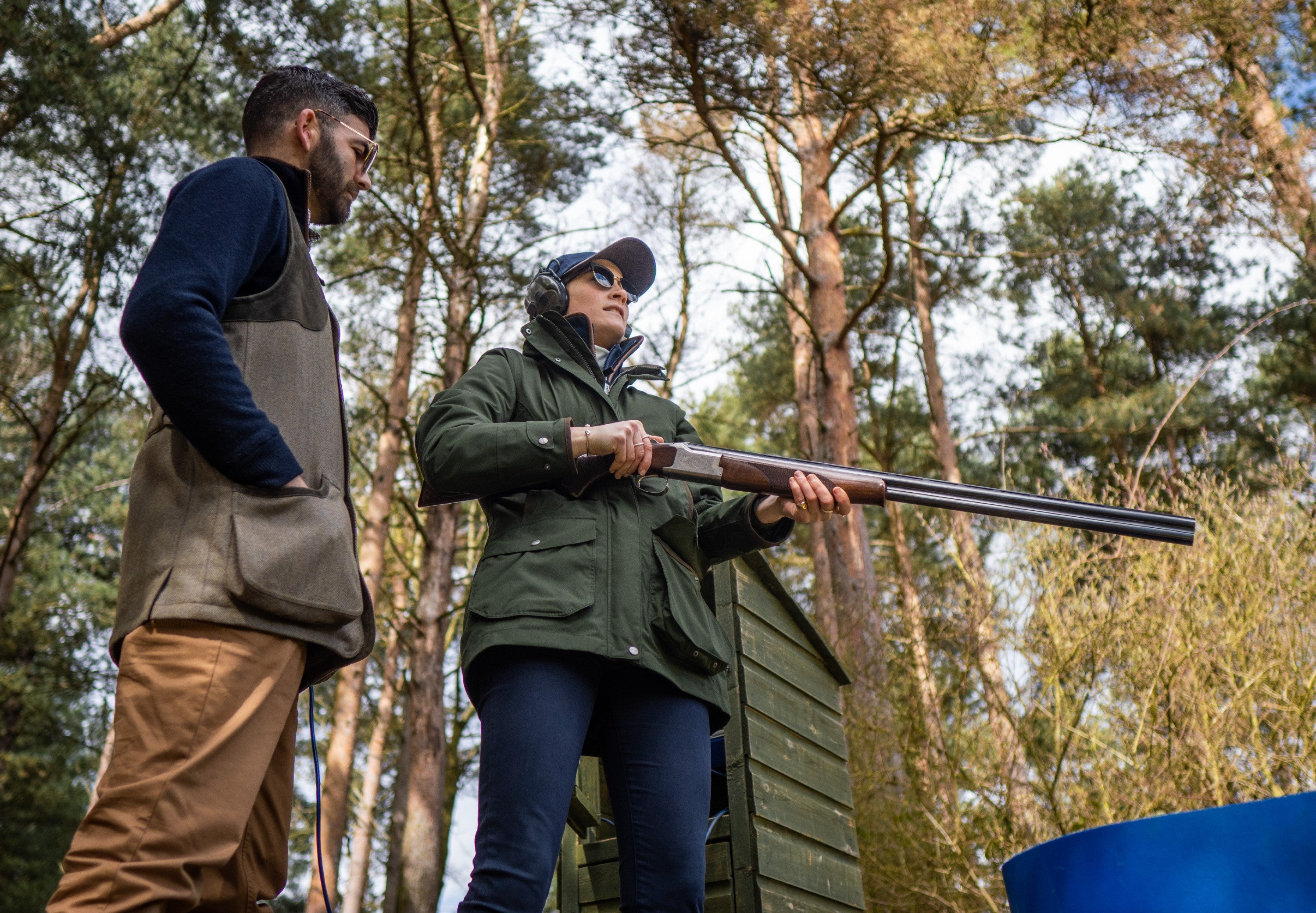 Two people in a forest setting, one holding a gun.
