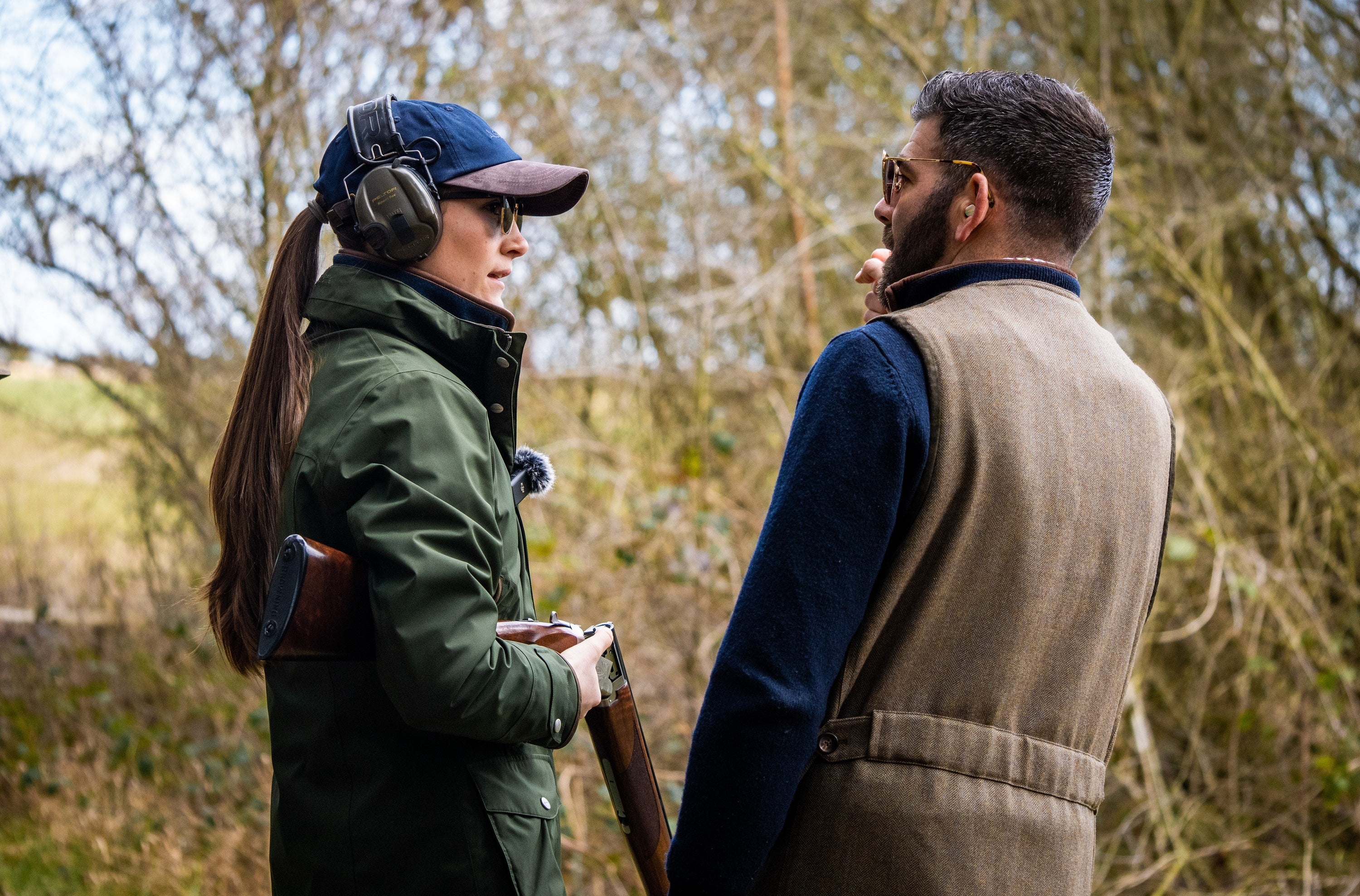 Two people in outdoor clothing with shooting gear in a natural setting