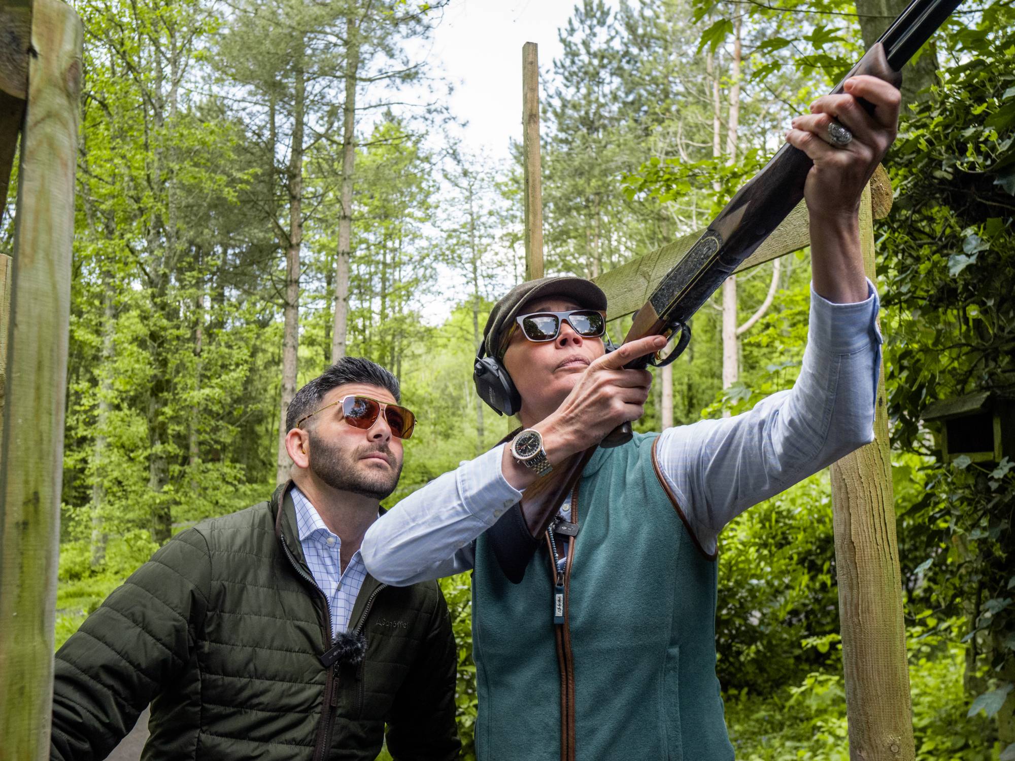 Two people in a forest setting, one holding a gun.