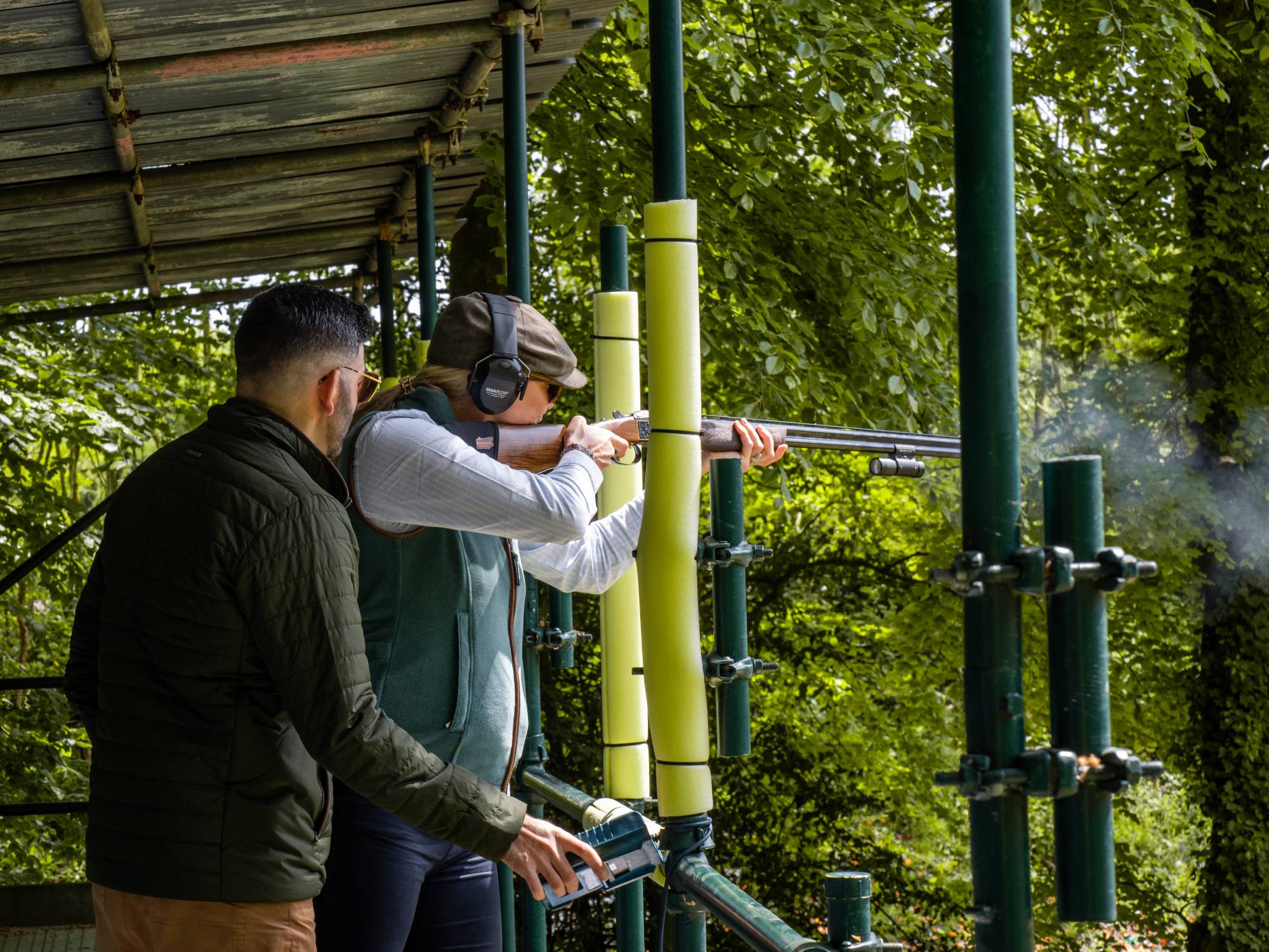 Two people on a shooting range with one person aiming a rifle.