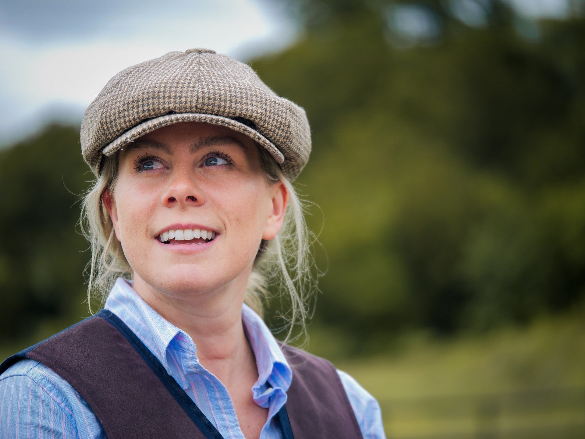 Woman wearing a checkered cap and vest outdoors with a blurred natural background