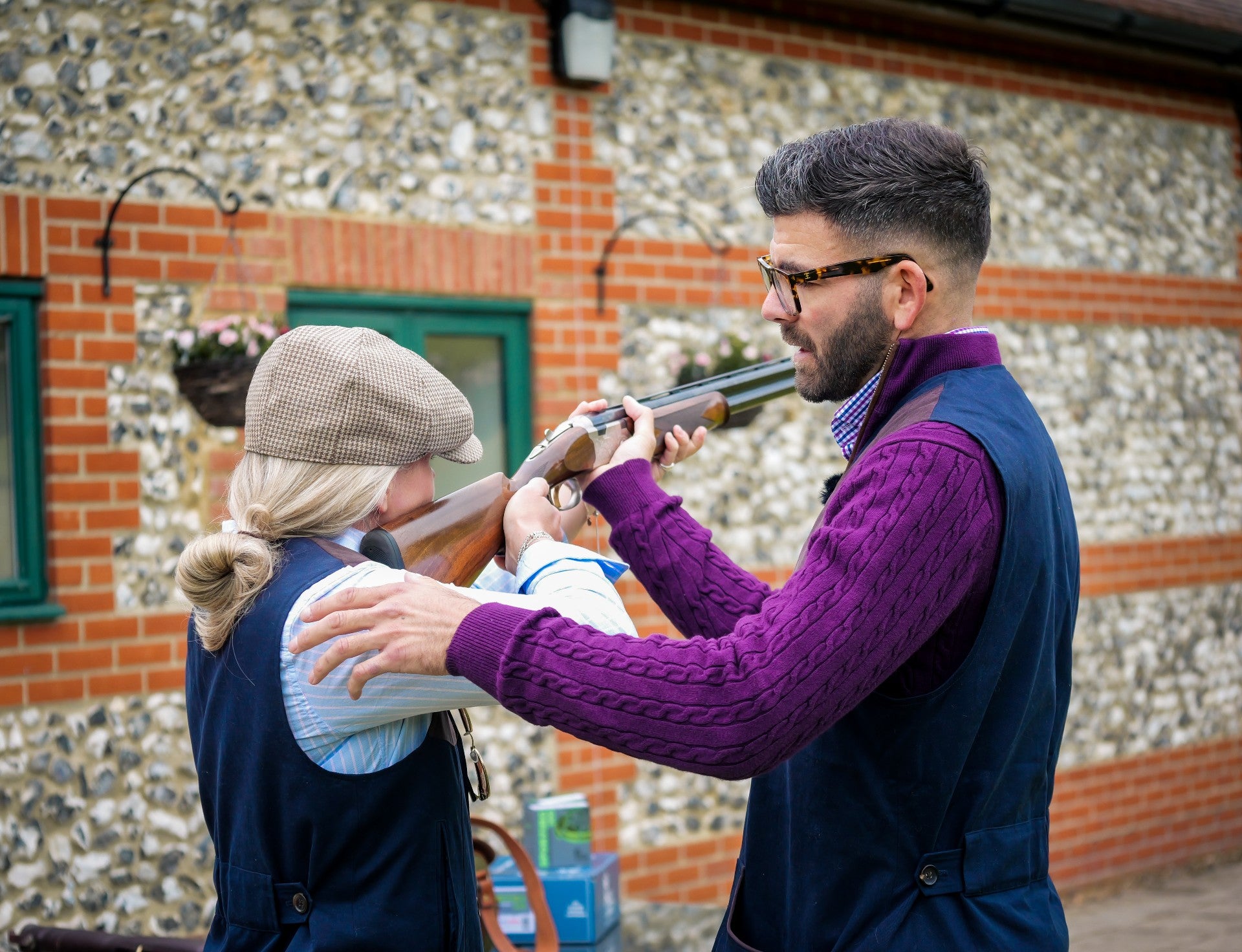 Man teaching a woman how to handle a shotgun outdoors.