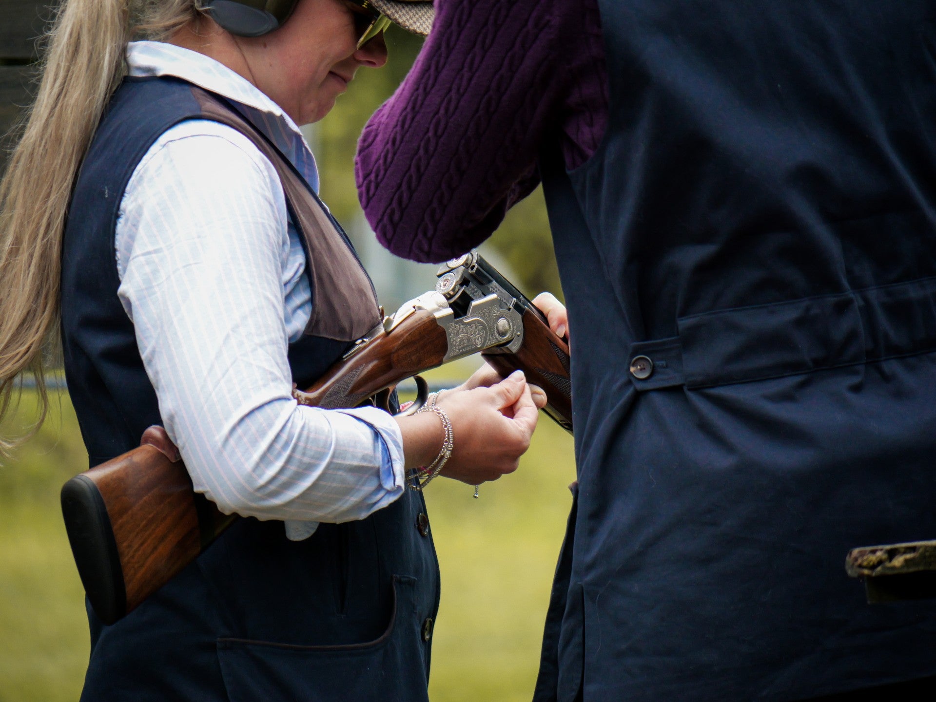 Two people interacting with a rifle in an outdoor setting