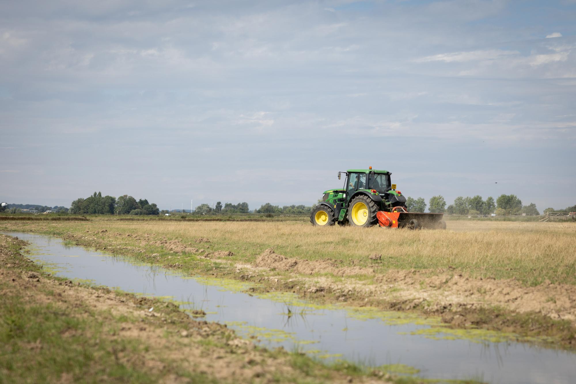 Tractor ploughing a field with water nearby under a clear sky