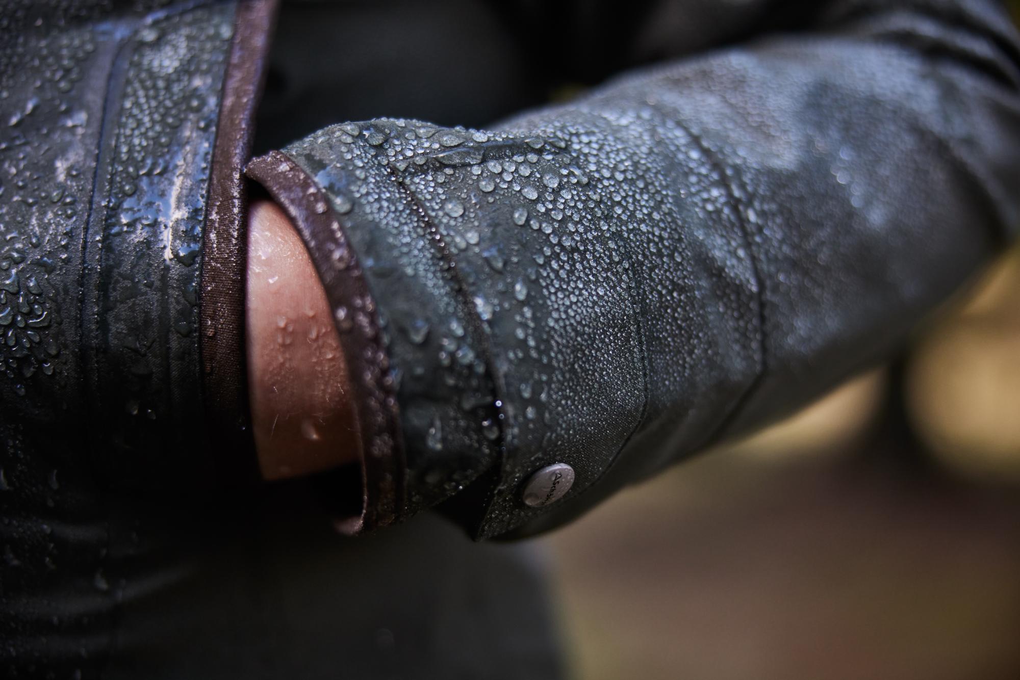 Close-up of a person wearing a dark jacket with water droplets on the sleeve, blurred background