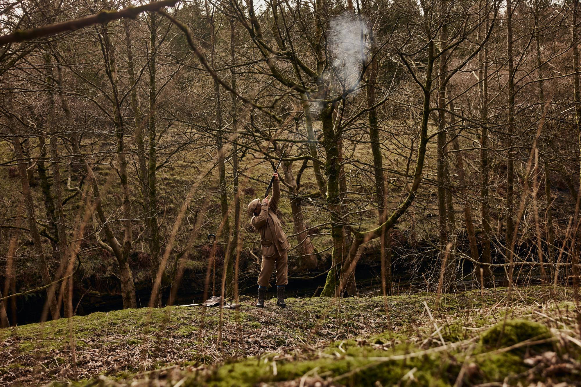 Person in a forest with smoke rising from a gun