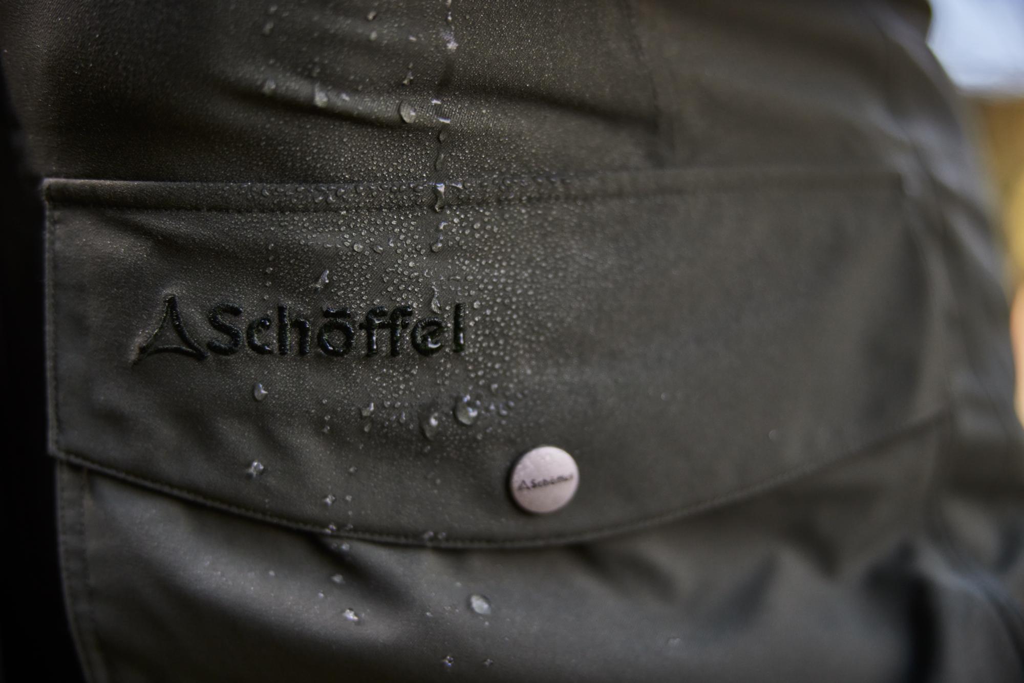 Close-up of a dark green jacket with 'Schöffel' branding and water droplets.