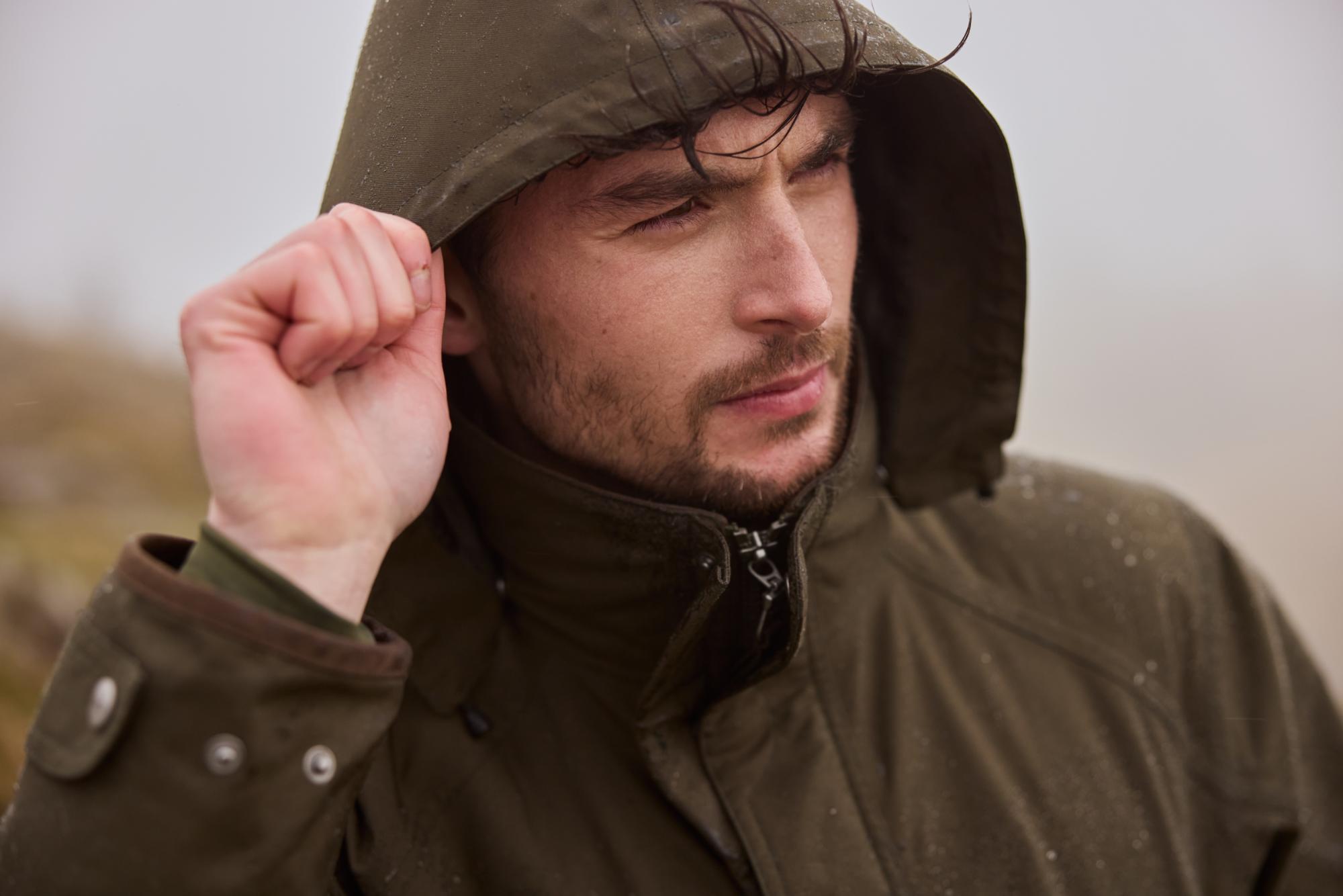 Man wearing a brown raincoat with a hood in a blurred outdoor setting