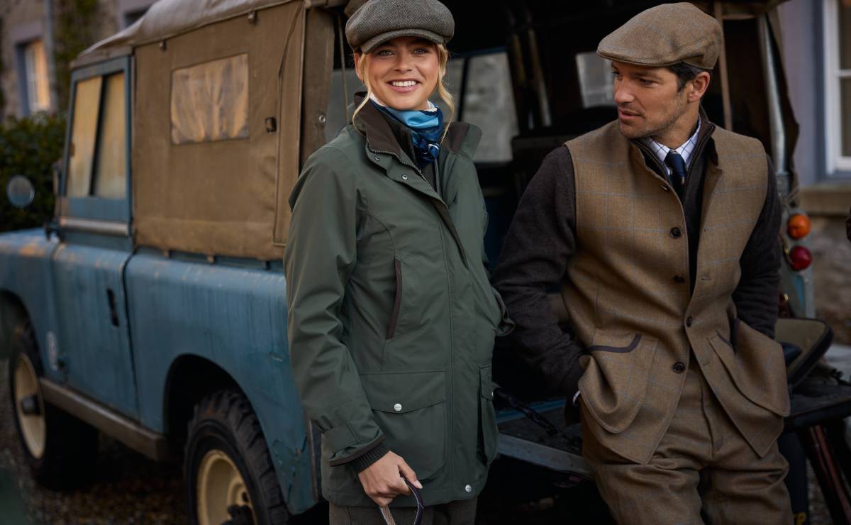 Two people standing in front of a vintage Land Rover, dressed in outdoor attire.