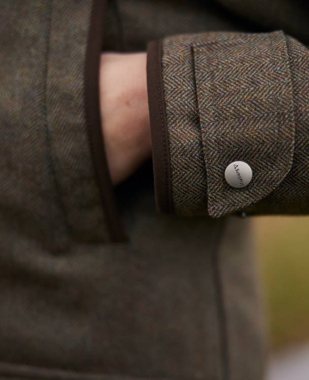 A close up image of a tweed jacket, image highlights the hand warming pockets and adjustable cuffs.
