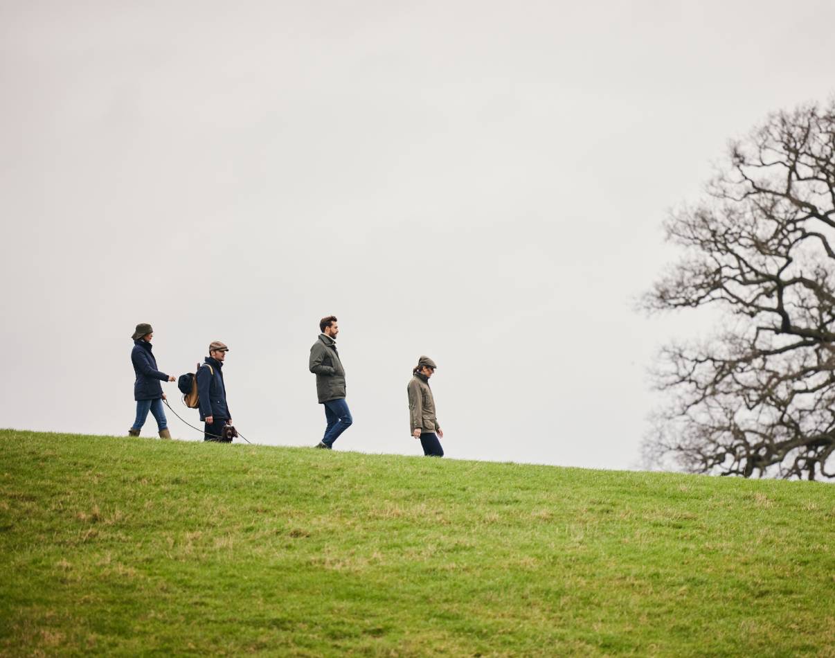 A group of people walking in a field wearing countrywear.