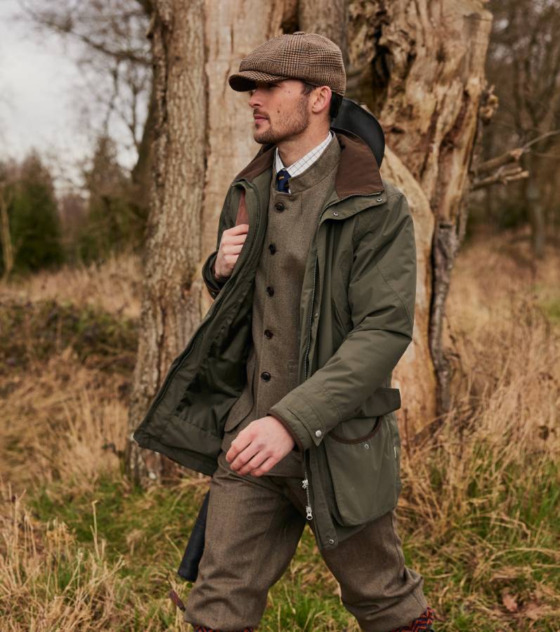 A man wearing countrywear walking in woodland.