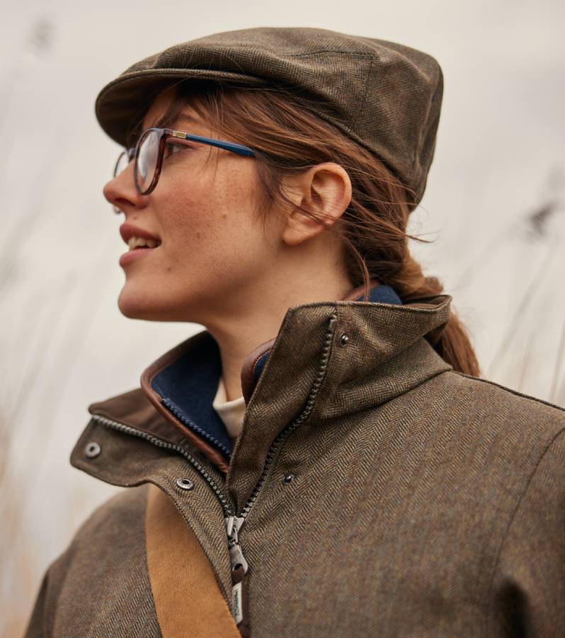 Close up image of lady wearing a tweed jacket with matching tweed cap. Image highlights the zip and collar detailing.