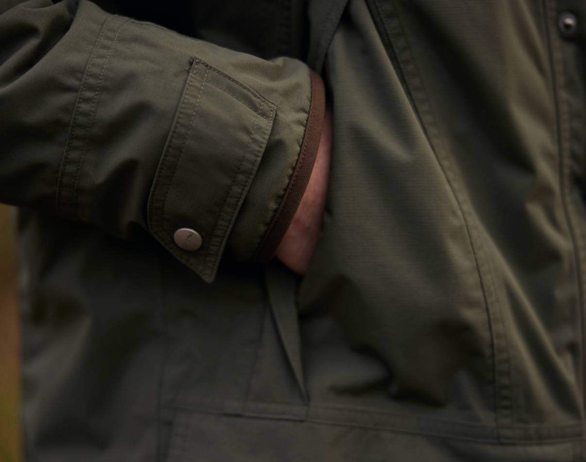 Close up image of a green waterproof jacket. Image highlights the hand warming pockets and adjustable cuffs.