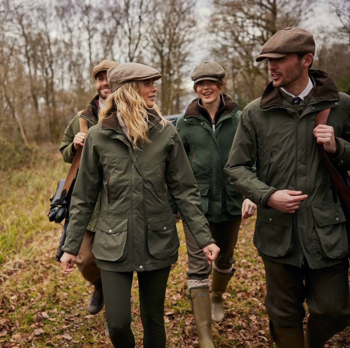 A group of people and dogs walking in a field wearing countrywear.