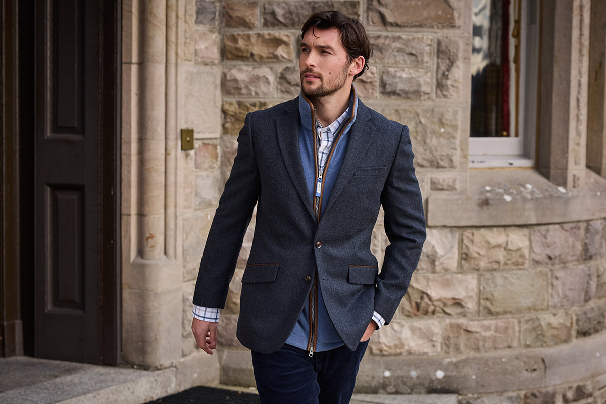 A man wearing a dark gray blazer over a blue shirt and patterned tie.