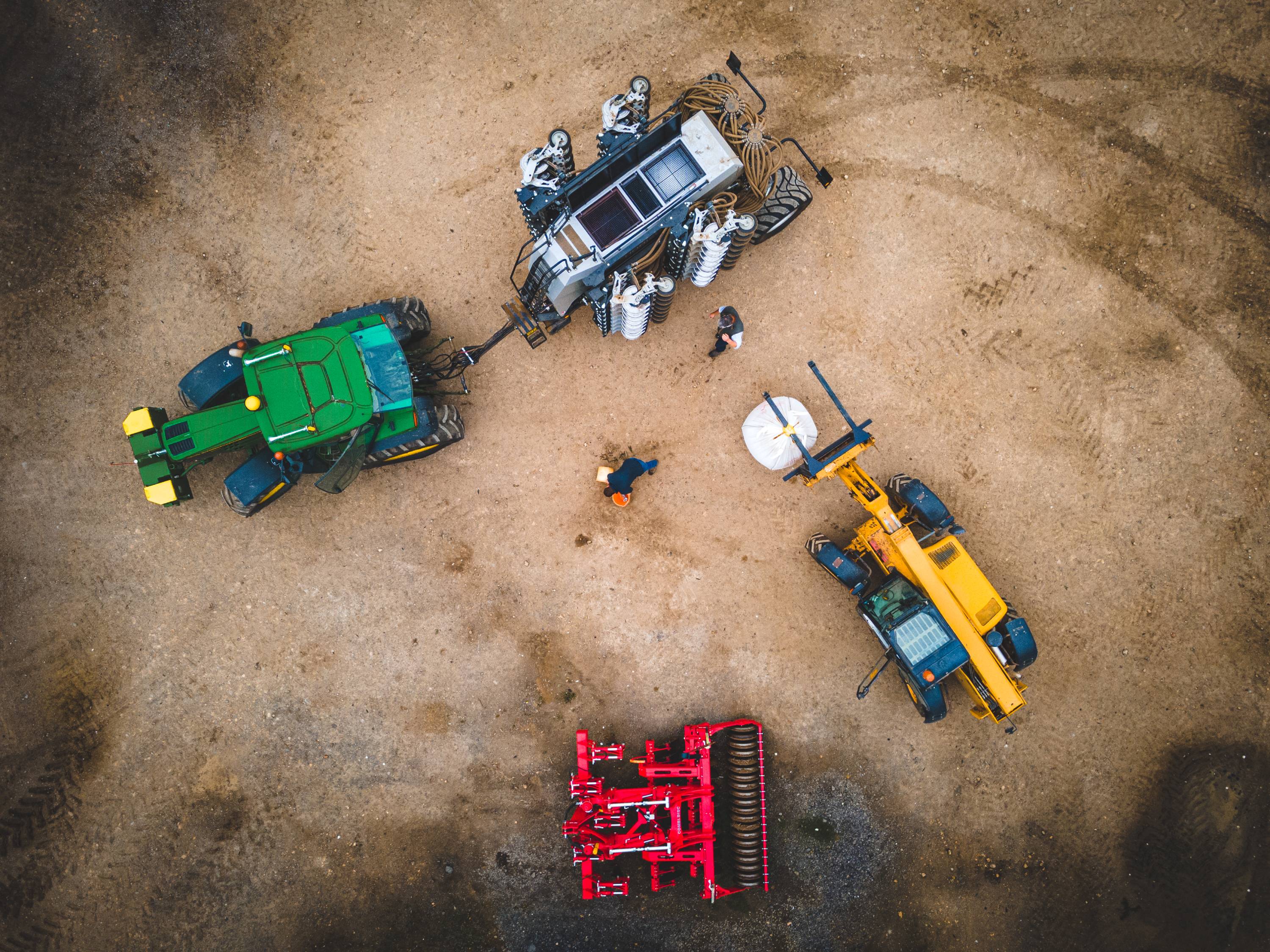 An ariel view of tractors and farmers in a field.