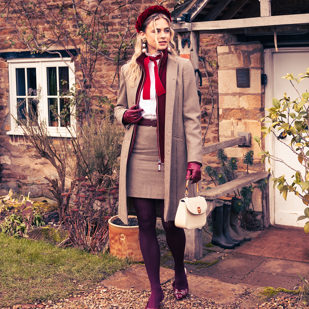A woman wearing a smart tweed jacket with dark red gilet and matching tweed skirt.
