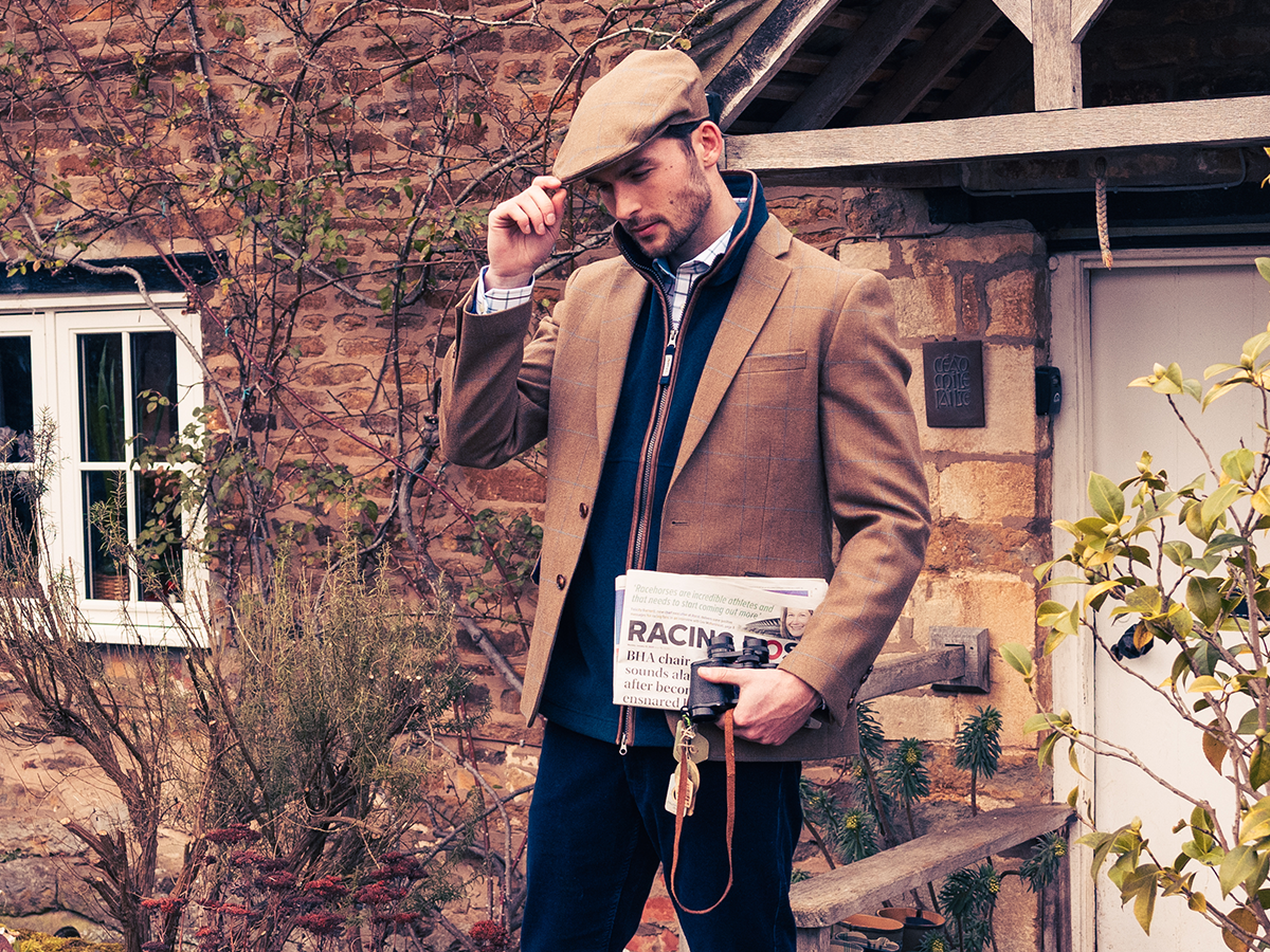 A man wearing a smart tweed jacket with navy gilet and blue trousers.