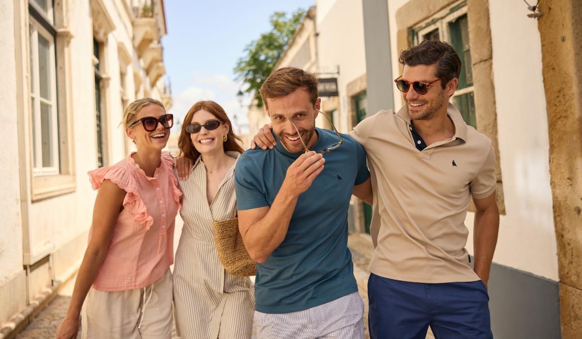 Four friends walking together on a sunny street, enjoying each other's company.