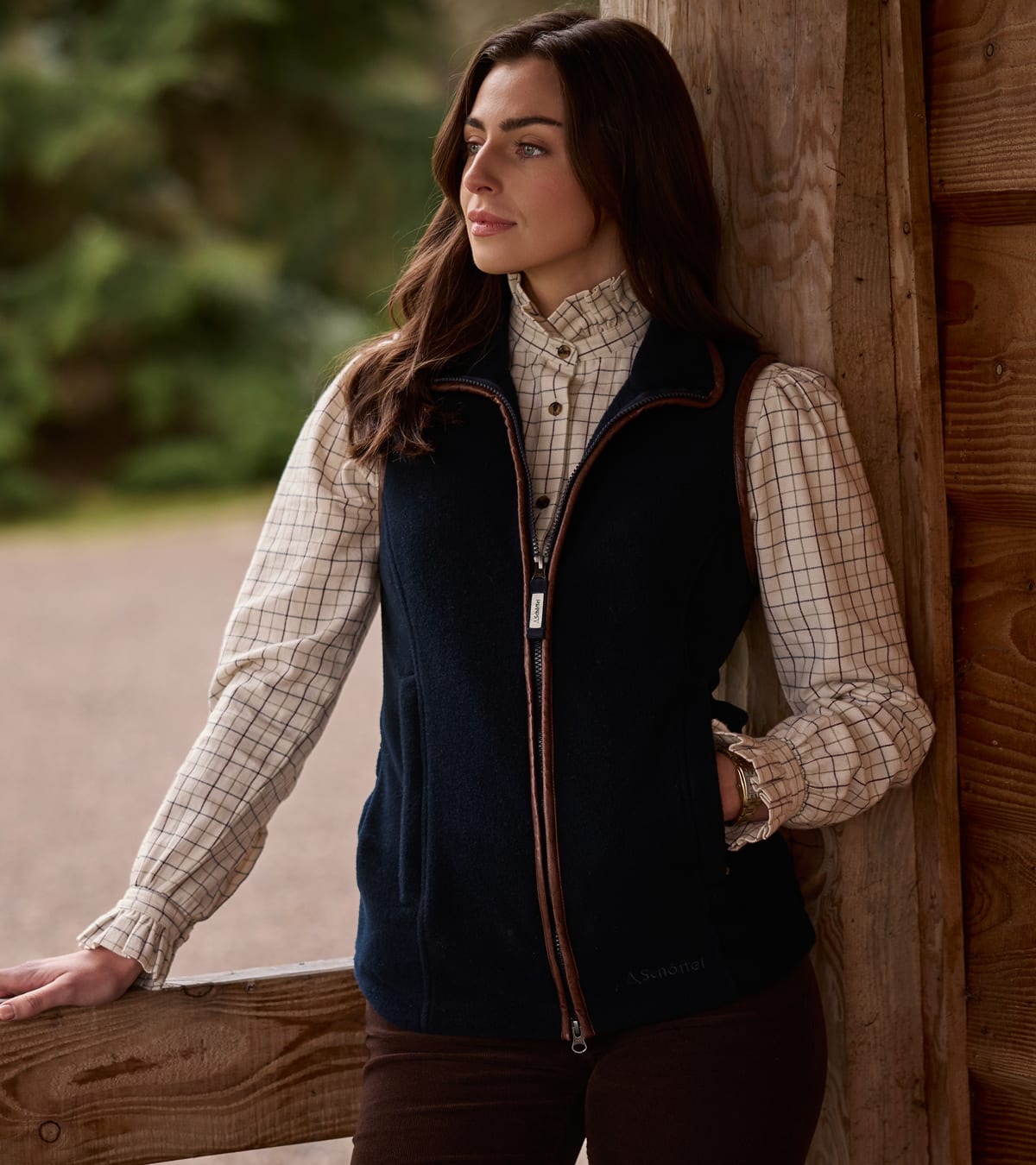 Woman wearing navy fleece gilet with brown leather trim over cream checked ruffle-collar blouse