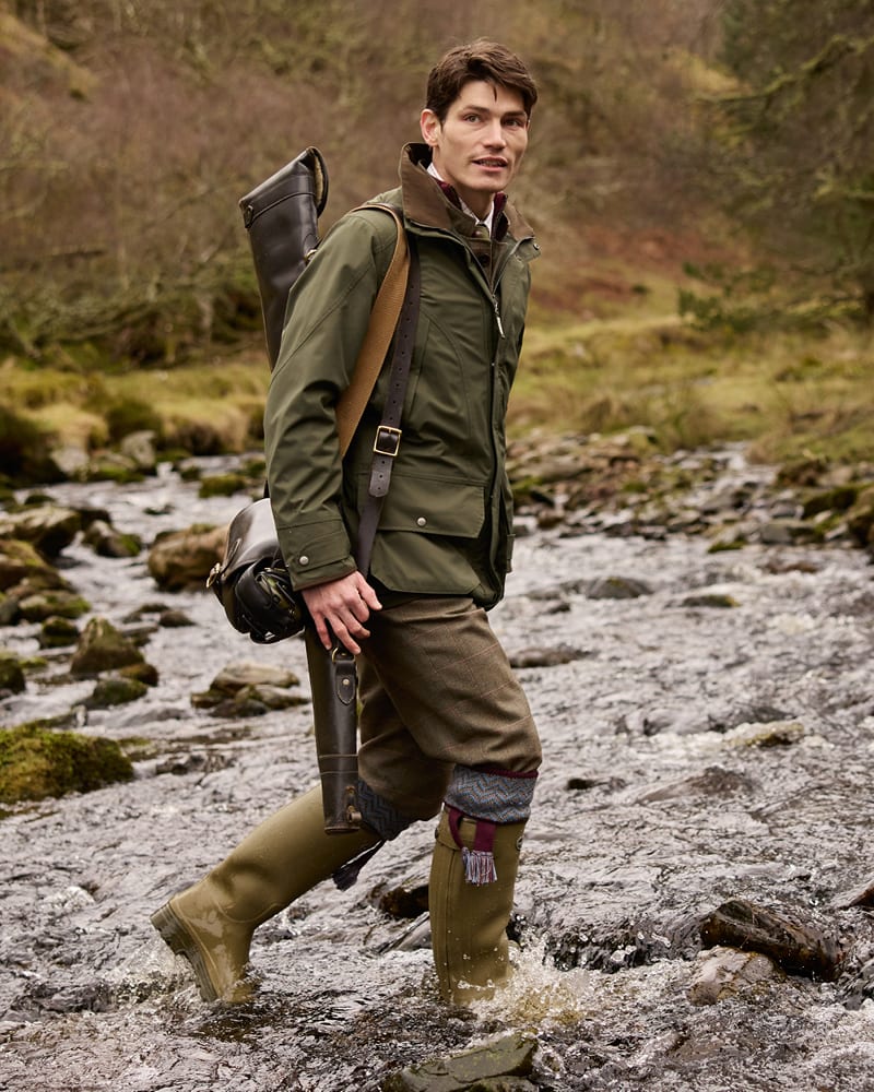 Man in olive green shooting jacket and tweed plus fours crossing a river