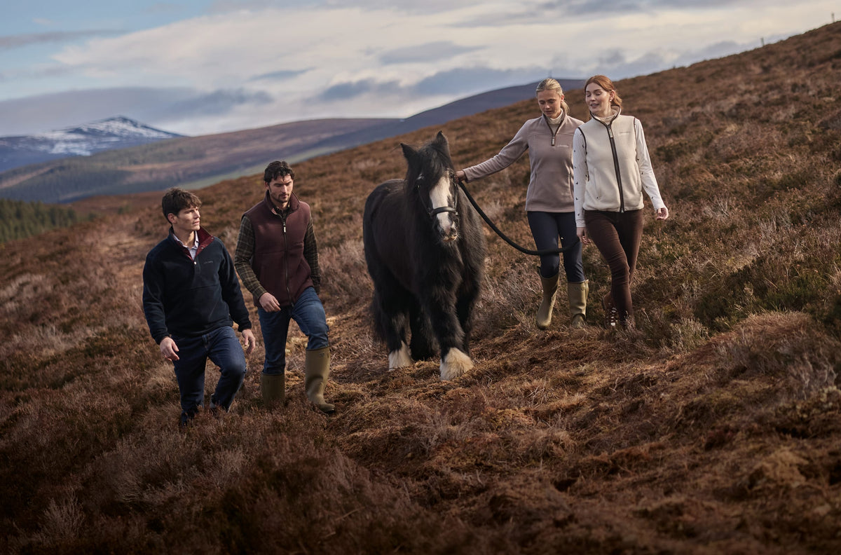 Four people walking across a grassy hillside with a large black horse.