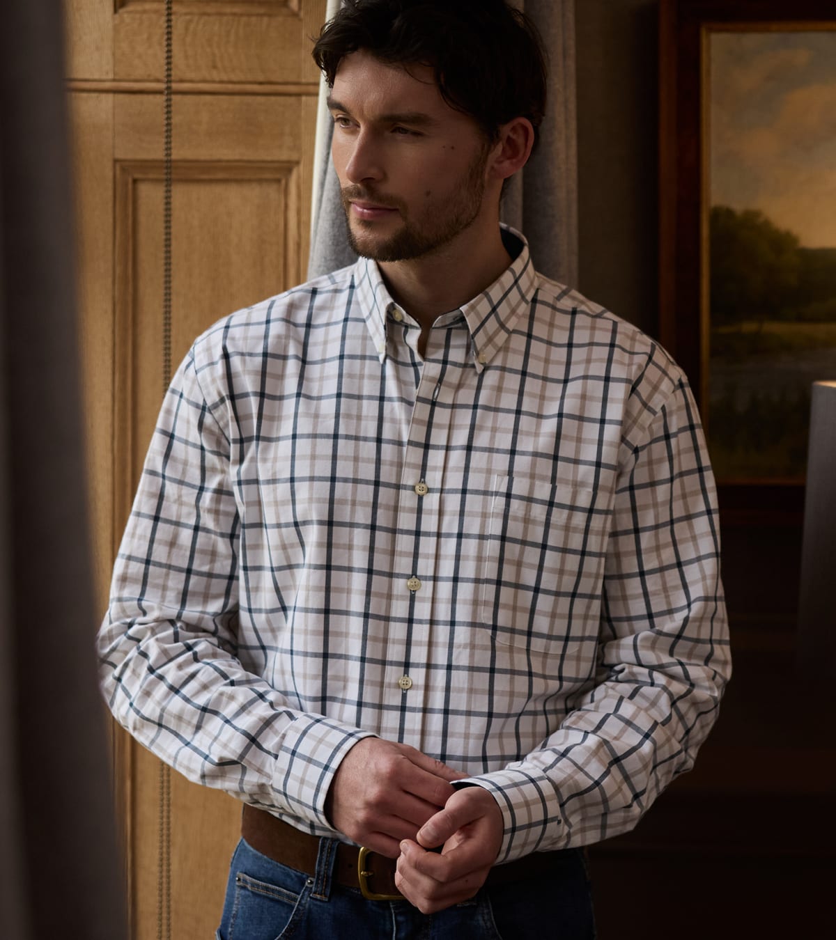 A man wearing a long-sleeve shirt, standing in a warmly lit indoor setting.