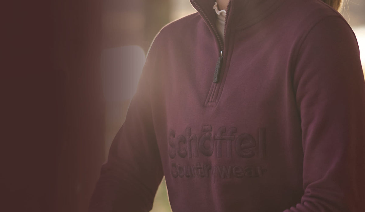 A close-up of a person wearing a burgundy quarter-zip sweatshirt with embroidered 'Schöffel Countrywear' logo