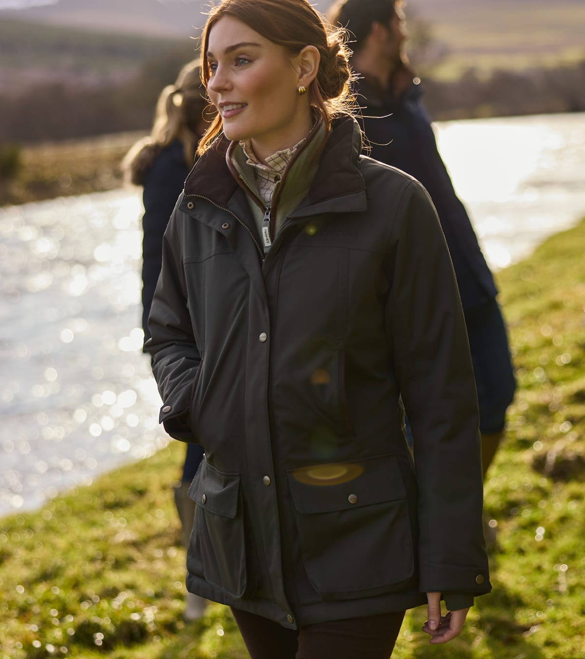 Woman walking along a riverbank wearing a dark green country coat