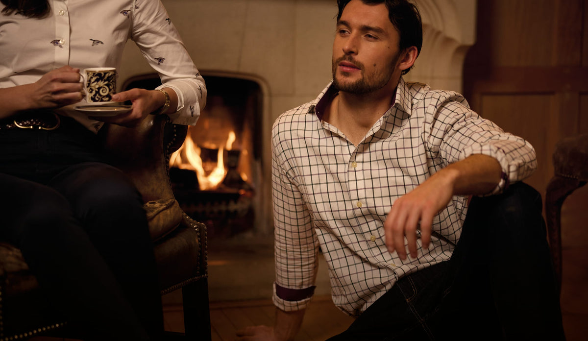 Man sitting by a fire wearing a cream shirt with a red and green checked pattern
