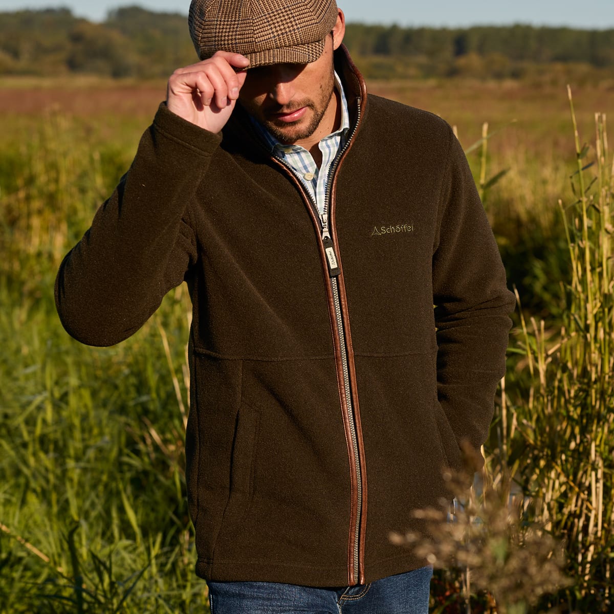 Man standing in a field wearing a green fleece jacket and tweed hat