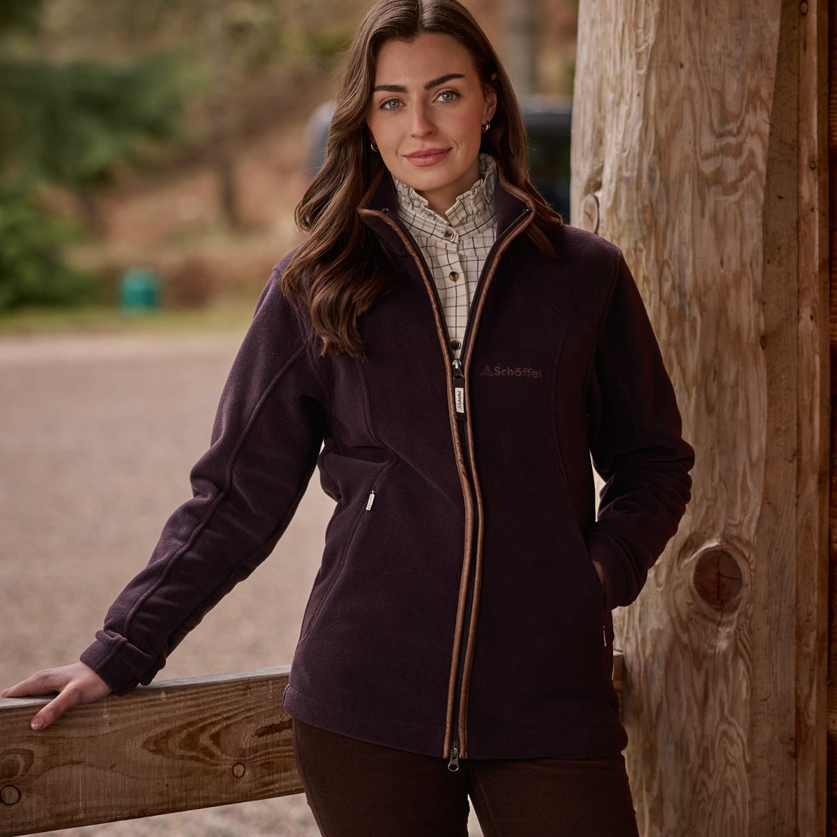 Woman standing near a log cabin wearing a port fleece jacket and cream checked shirt